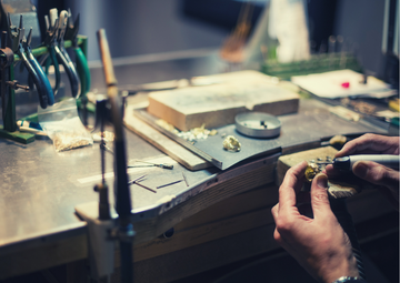 Artesan making a ring by hand in front of a table where he crafts his jewels