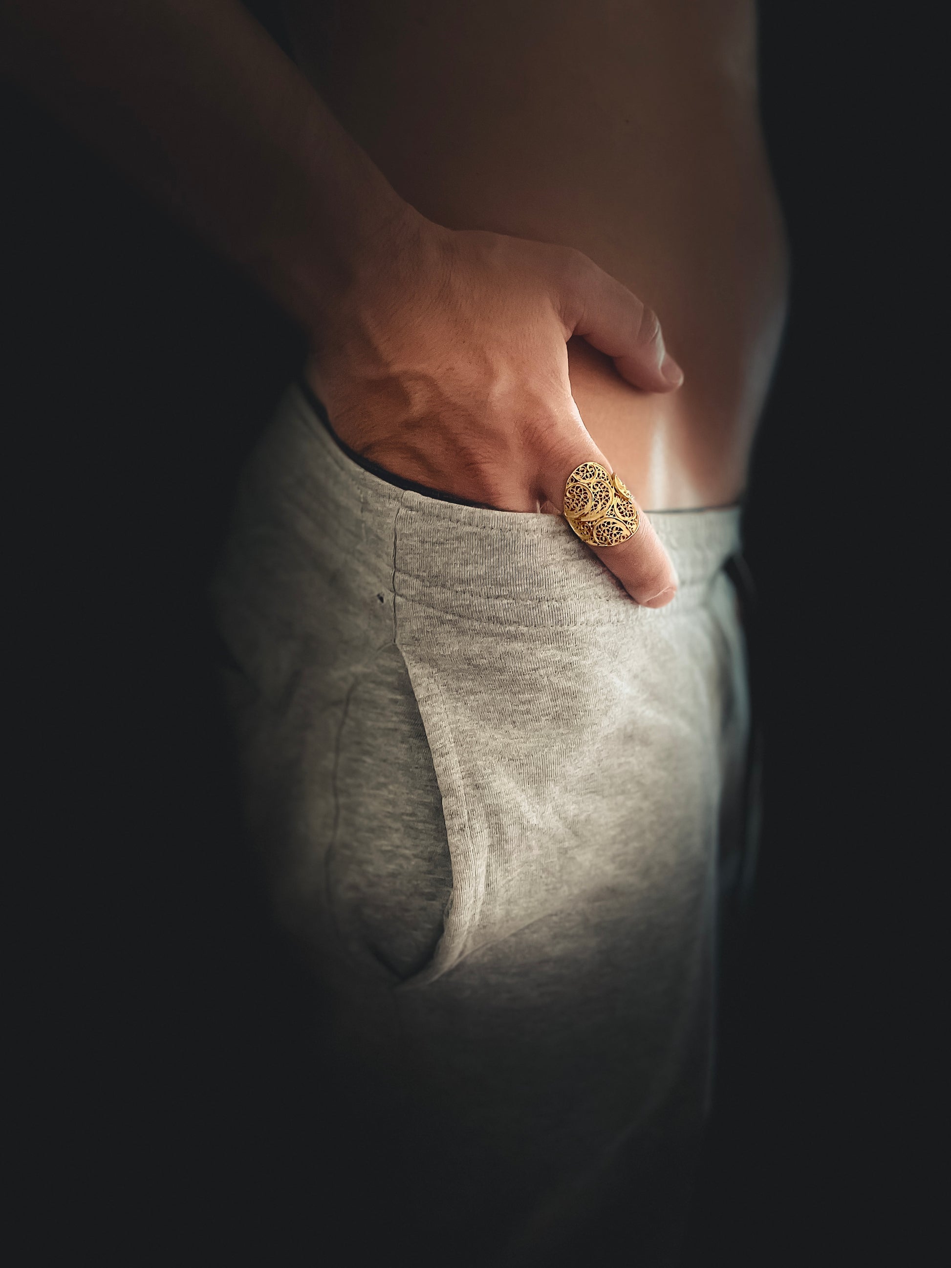 Man using grey shorts, showing his hand using a filigreee gold ring named  Sexy and They Know it ring, made by Estorya Store.